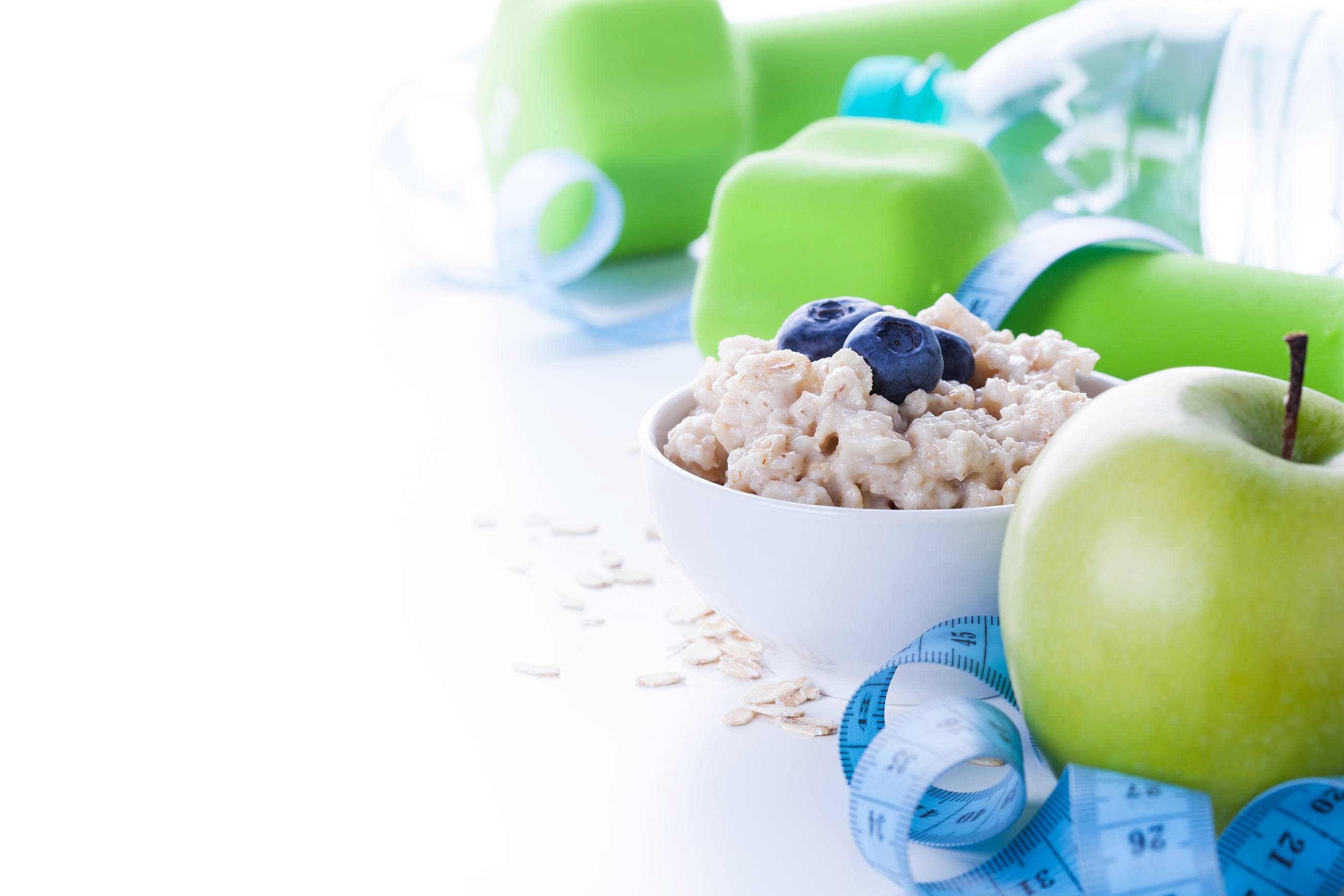 Fitness frame with energy breakfast oatmeal apple and mineral water with sport tools on background. Healthy weight loss concept with copy space.