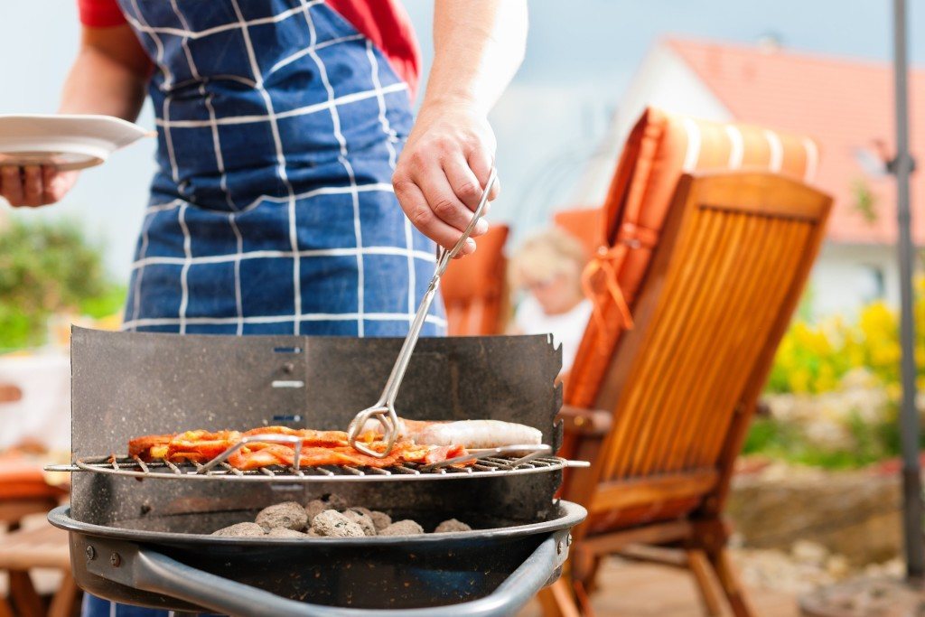 Happy family having a barbecue in summer; father stands next to the fire