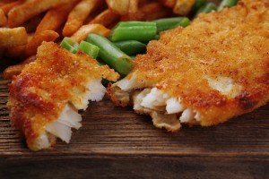 Breaded fried fish fillet and potatoes with asparagus on wooden cutting board background