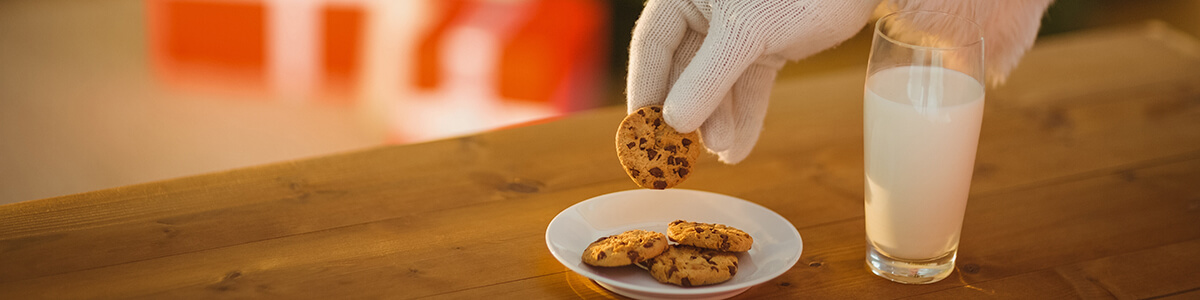 Santa Claus reaching for a plate of cookies and milk that were left out for him.