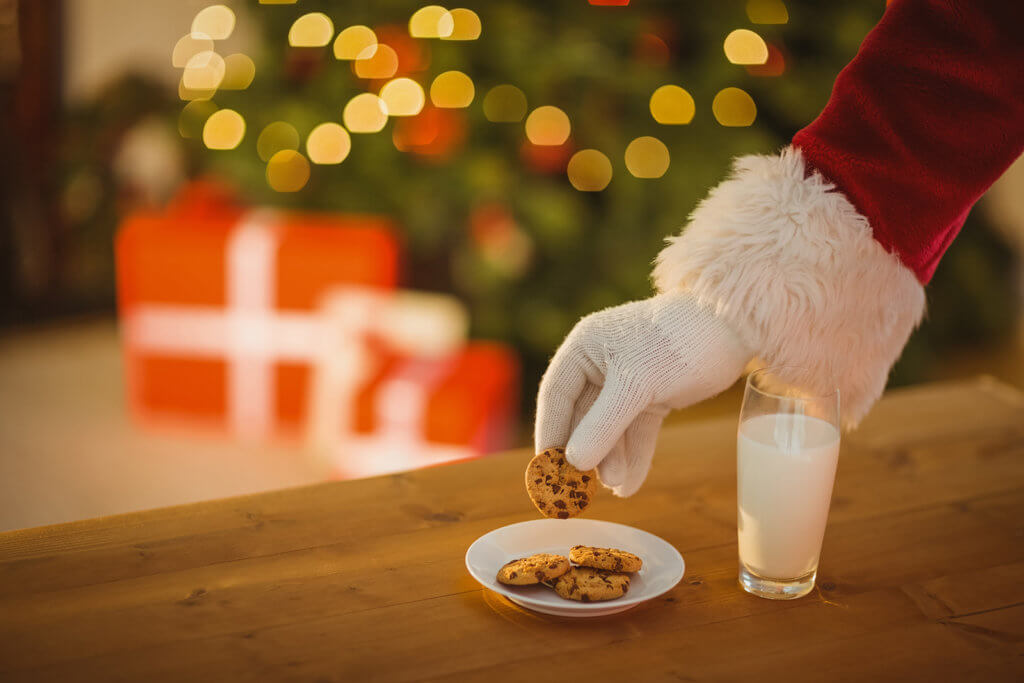 Santa Claus reaching for a plate of cookies and milk that were left out for him.