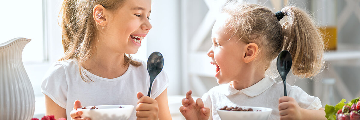 Two young girls sitting at the table eating breakfast