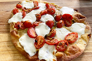 a flatbread pizza with cut up tomatoes, melted cheese and hummus spread