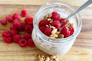 a cup of oats with peanut butter, crushed peanuts and raspberries